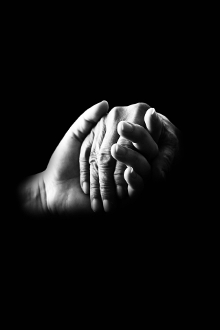dłoń młodej osoby przytrzymuje dłoń starszej osoby, zdjęcie w kolorach szarości 