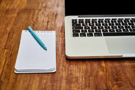 notatnik z niebieskim długopisem i otwarty laptop na drewnianym stole 